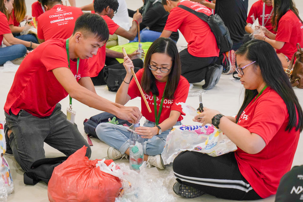 Youth Corps members stuffing a plastic bottle with plastic waste using a stick to make an ecobrick (Photo by Chan May Ching) 